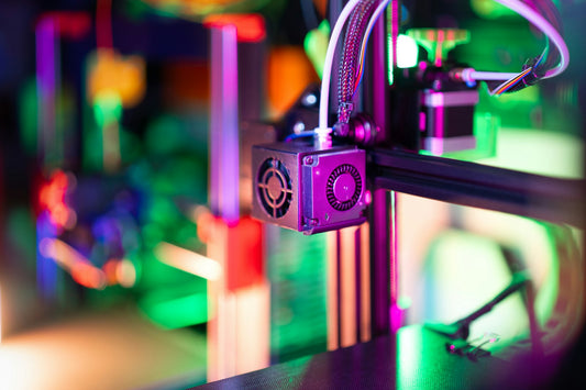 Close-up of a 3D printer hotend and nozzle in a colorful maker workshop
